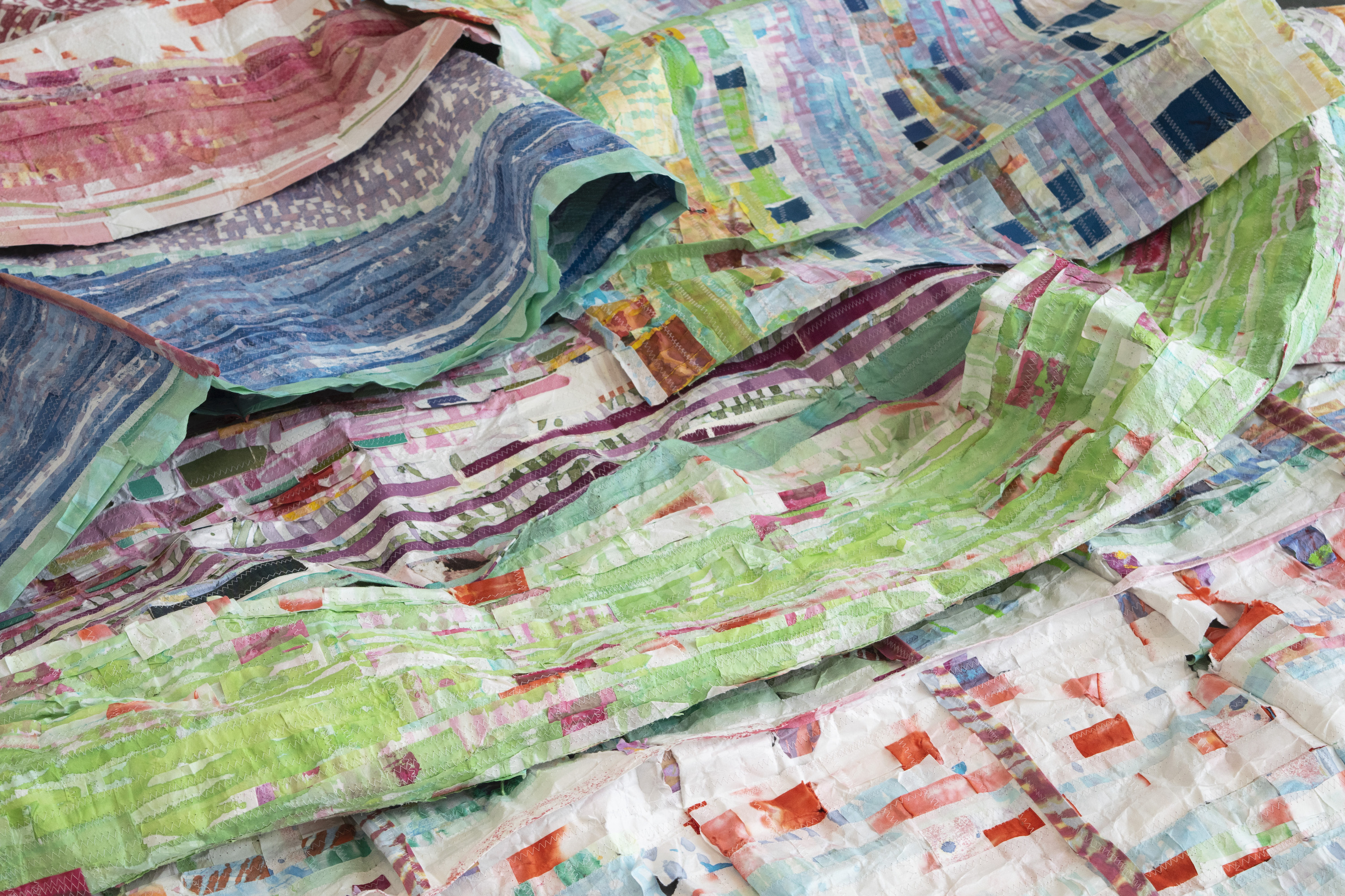 Photograph of several sewn paper quilt collages overlapping on the floor