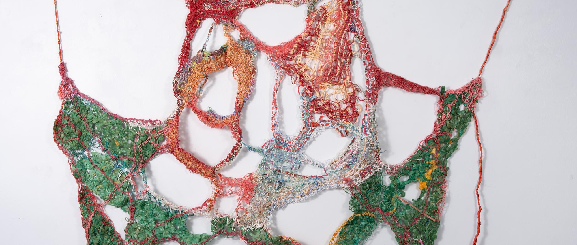 Net-like crocheted artwork made of handspun paper hung on a white wall